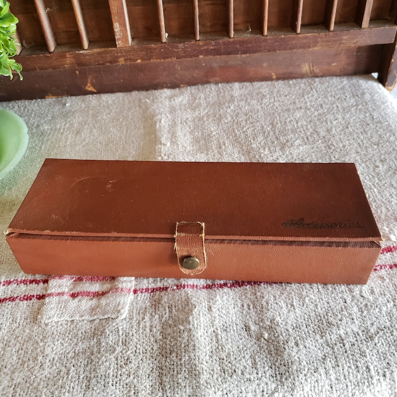 May include: A brown leather box with a brass clasp and the word "Accessories" embossed on the top.