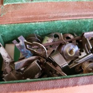May include: A close-up of a collection of vintage sewing machine parts in a green and brown velvet box. The parts are made of metal and have a worn, rusty appearance.
