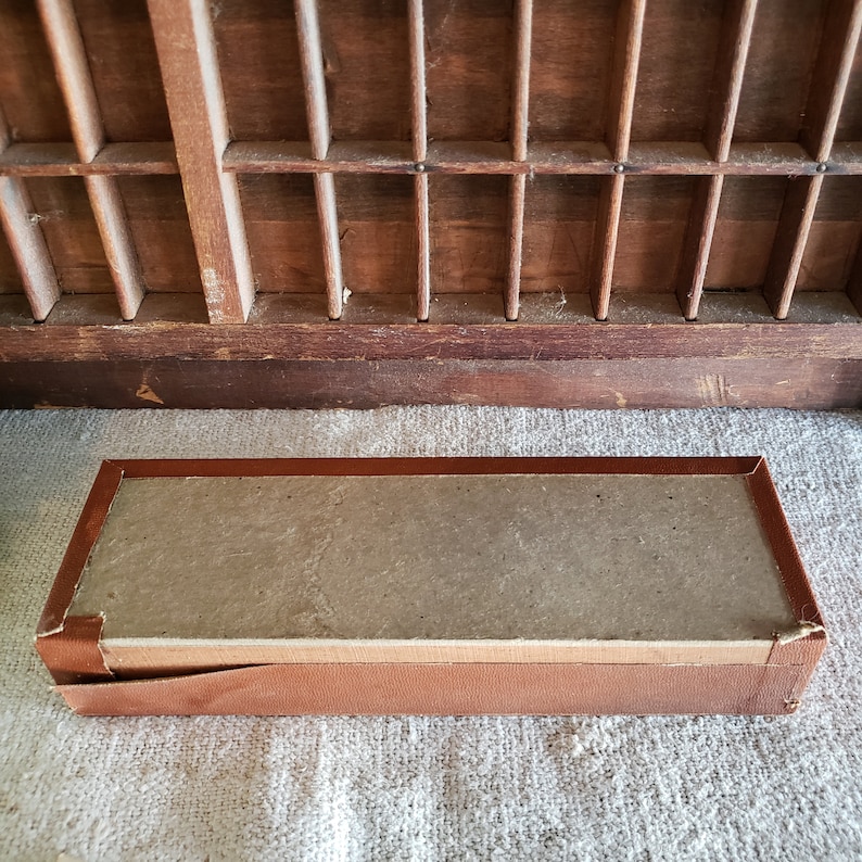 May include: A brown cardboard box with a brown leather trim. The box is empty and has a textured surface.