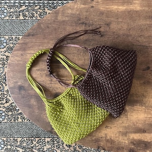 Könnte beinhalten: Zwei kleine, handgefertigte Häkeltaschen mit einem strukturierten Webmuster. Eine Tasche ist in einem leuchtenden Limettengrün gehalten, die andere in einem tiefen Dunkelbraun. Jede Tasche hat einen passenden geflochtenen Kordelgriff.