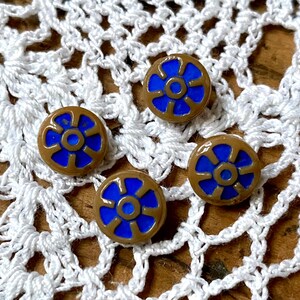 May include: Four brown and blue glass buttons with a flower design. The buttons have a raised rim and a center circle.