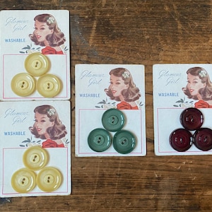 May include: Four cards with a vintage design featuring a woman's face and the text "Glamour Girl Washable". Each card has three buttons in different colors: yellow, green, and maroon.