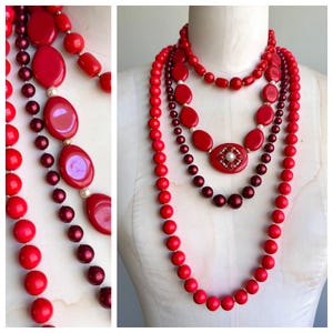 May include: A collection of red necklaces displayed on a mannequin. The necklaces vary in style, including beaded strands and pieces with oval and round accents. Some necklaces feature a mix of red and burgundy beads, with a central pendant.