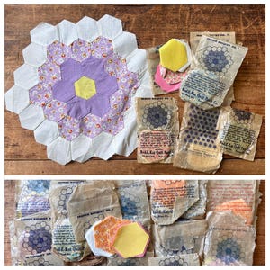 May include: A collection of hexagonal fabric quilt patches featuring a central yellow hexagon surrounded by purple and floral patterned hexagons, bordered by white. Includes several vintage paper packets labeled Red-E-Kut Quilt Patch Co.