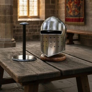 May include: A polished metal knight's helmet with a visor and ventilation holes, displayed on a wooden stand. A black helmet stand is to the left. The helmet sits on a wooden table in a stone room.