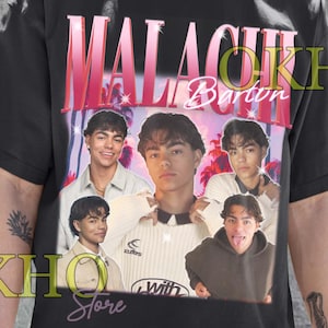 May include: Black unisex t-shirt with a graphic of a young man, the name "Malachi Barton" in pink and white text, and multiple images of the same person. The words "Unisex T-Shirt" are printed at the bottom of the shirt.