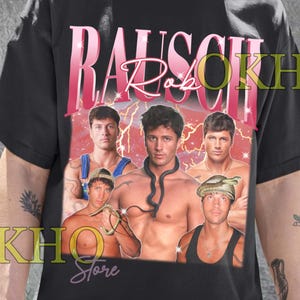 Puede incluir: Camiseta unisex negra con un diseño gráfico. El diseño presenta el texto "RAUSCH Rob" en rosa y blanco, junto con imágenes de varios hombres. Es una prenda de vestir informal.