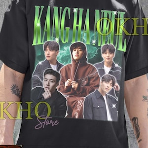 May include: Black unisex t-shirt featuring a graphic of a musical group with the text "KANG HA NEUL" in green. The shirt also has the text "OKHO Store" and "Unisex T-Shirt".