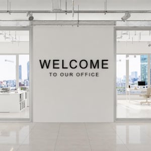 Könnte beinhalten: Modernes Bürointerieur mit einer weißen Wand mit dem Text "WELCOME TO OUR OFFICE" in Schwarz. Der Raum umfasst Büros mit Glaswänden, Schreibtischen, Stühlen und Stadtansichten, wodurch eine helle und professionelle Atmosphäre entsteht.