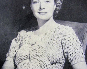 May include: A woman wearing a crocheted top with a delicate openwork pattern. The top has a V-neckline and short sleeves. The woman is sitting in a chair and has her hands in her lap.