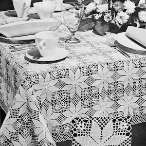 Puede incluir: Un mantel de crochet blanco con un delicado patrón floral. El mantel está puesto sobre una mesa con platos y vasos blancos, y un ramo de flores blancas está en el fondo.