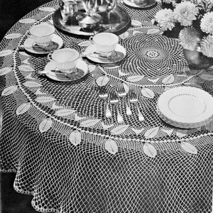 May include: A white crocheted tablecloth with a delicate leaf pattern and a scalloped edge. The tablecloth is set with a teapot, cups, saucers, and silverware.