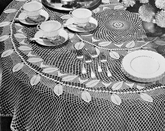 May include: A white crocheted tablecloth with a delicate leaf pattern and a scalloped edge. The tablecloth is set with a teapot, cups, saucers, and silverware.