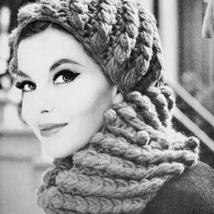 May include: A close-up of a woman wearing a gray knitted hat and matching scarf. The hat is a slouchy style with a wide brim and the scarf is a thick, chunky knit.