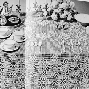 May include: A black and white photo of a table setting with a white crocheted tablecloth, silver teacups and saucers, a silver teapot, and silver candlesticks.