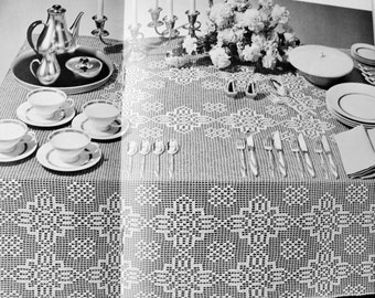 May include: A black and white photo of a table setting with a white crocheted tablecloth, silver teacups and saucers, a silver teapot, and silver candlesticks.