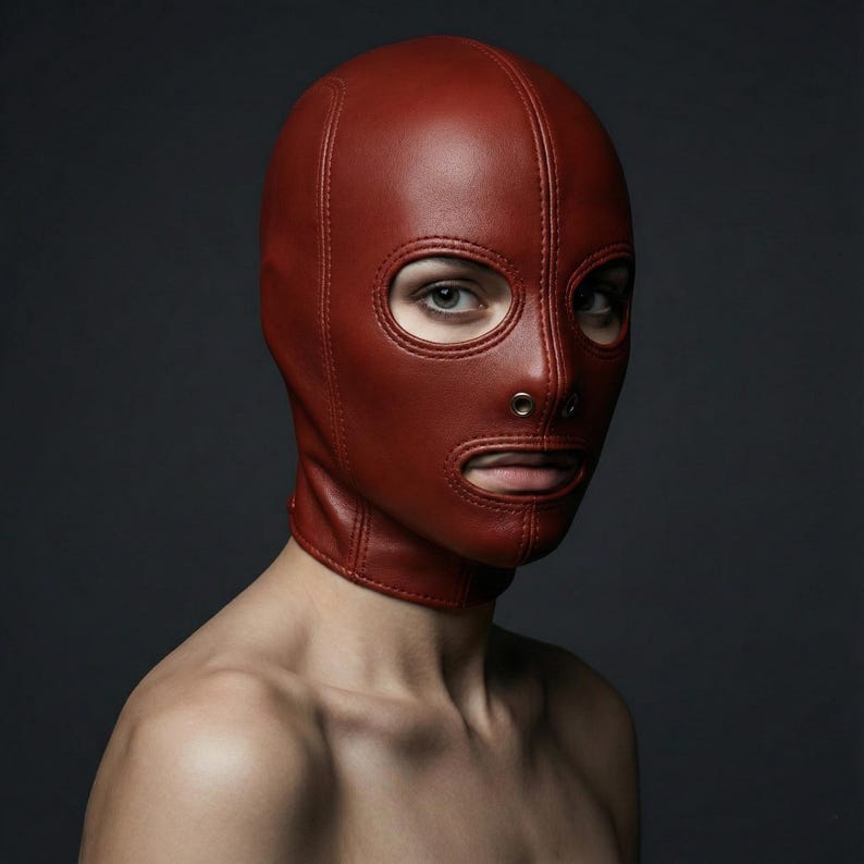 May include: A red leather hood with eye and mouth openings. The hood features a neck collar and is stitched along the seams. The background is a dark grey.