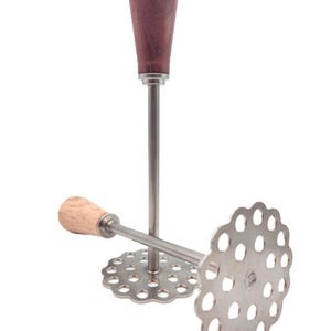 May include: A stainless steel potato masher with a wooden handle. The masher has a circular head with multiple holes for mashing potatoes. The handle is dark brown and the other handle is light brown.
