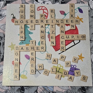 May include: A festive Christmas-themed artwork featuring a crossword puzzle with holiday words like "Rudolph" and "Reindeer." The artwork includes a drawing of Santa's sleigh, Christmas tree, and the words "Happy Holidays."