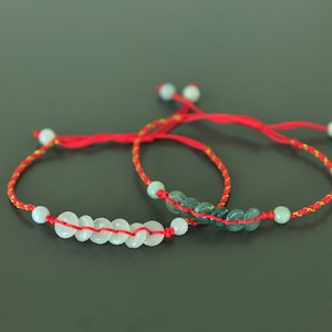 Könnte beinhalten: Zwei rote Armbänder mit Jadeperlen. Ein Armband hat weiße Jadeperlen und das andere hat grüne Jadeperlen.
