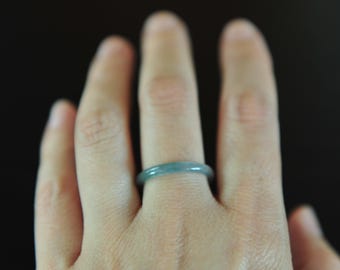 May include: A smooth, solid band ring crafted from a translucent, pale blue-green stone. The ring features a simple, rounded profile with a polished finish, showcasing the natural color variations and subtle internal texture of the material.