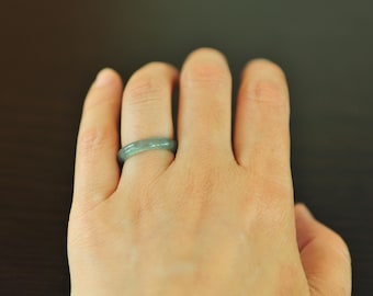 May include: A smooth, solid band ring crafted from a translucent, pale green stone material. The ring features a rounded profile and a polished surface, displaying subtle variations in color and tone throughout the circular band structure.