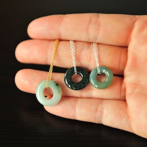 May include: Three circular stone pendants in shades of light green, dark green, and mottled green, each suspended from a delicate metal chain. One pendant hangs from a gold-toned chain, while the other two hang from silver-toned chains.