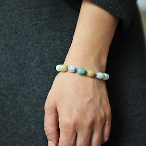 Könnte beinhalten: Ein Armband aus hellgrünen, gelben und weißen ovalen Perlen, die auf einer dunkelblauen Schnur aufgefädelt sind.