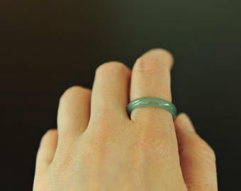 May include: A jade ring with a smooth, polished surface. The ring is a pale green color and is worn on a finger. The ring is a simple band design, showcasing the natural beauty of the jade.