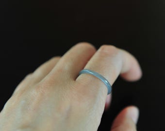 May include: A smooth, thin, solid band ring in a muted, cool-toned slate blue color. The ring features a simple, rounded profile with a consistent thickness throughout, showcasing a polished, semi-translucent finish that catches the light.