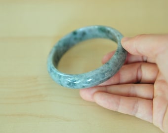 May include: A jade bangle bracelet with a light green and white colour. The bangle is smooth and polished.