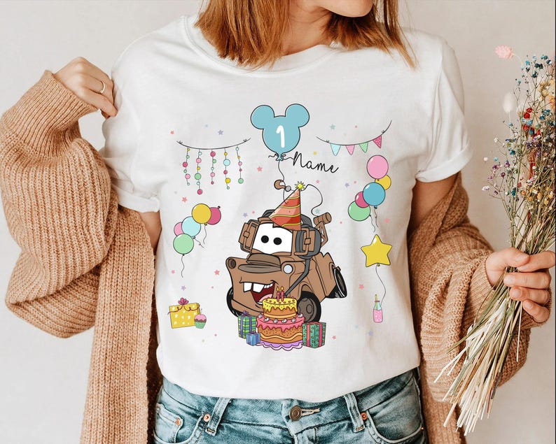 May include: White t-shirt featuring a cartoon image of Tow Mater from the movie Cars, wearing a party hat and surrounded by balloons and a birthday cake. The number 1 and the word "Name" are also included in the design.