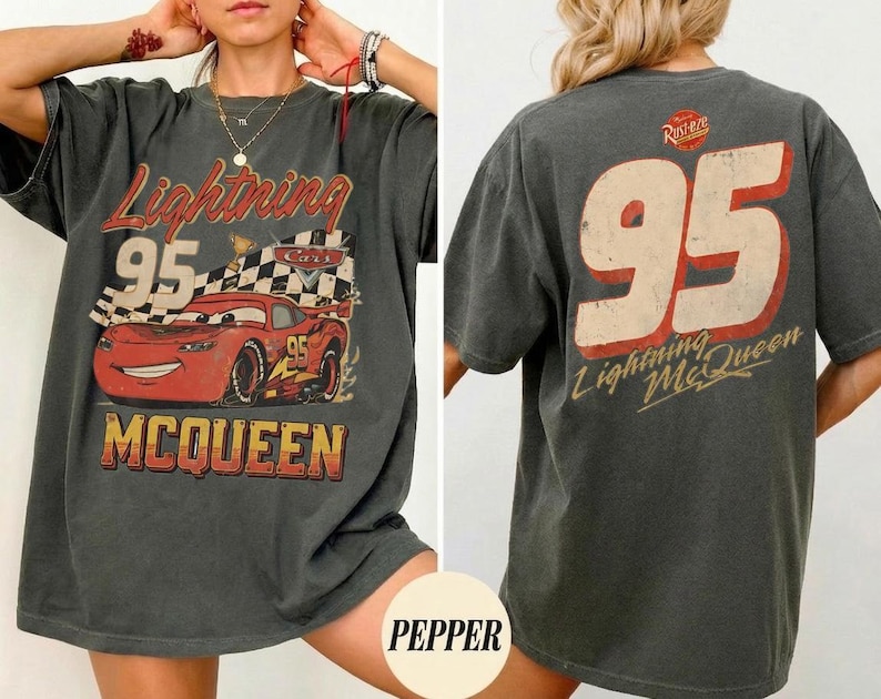May include: Dark gray t-shirt featuring a graphic of Lightning McQueen from the Cars movie. The front displays the number 95, the character's name, and a checkered flag. The back of the shirt also features the number 95 and the Lightning McQueen name.