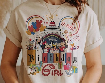 Puede incluir: Camiseta beige con un gráfico colorido de personajes de Disney en un crucero. El diseño incluye a Mickey y Minnie Mouse, el Pato Donald y Chip y Chop, con las palabras "Birthday Girl" y "Name". Globos y fuegos artificiales completan el look festivo.