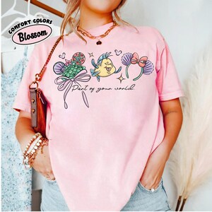 May include: A white ceramic mug with a black handle and the text "But First, Coffee" in a bold, black font. The mug is set against a blurred background. The mug appears to be approximately 10 cm tall.