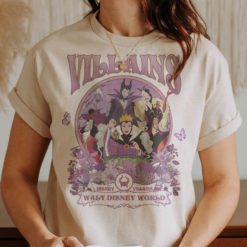 May include: Beige t-shirt featuring a purple graphic of Disney villains, including Maleficent and the Evil Queen, surrounded by flowers. The word "VILLAINS" is arched above the characters, with "WALT DISNEY WORLD" below.