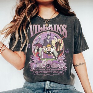 May include: Dark gray t-shirt featuring a purple graphic of Disney Villains. The design includes characters like Ursula, Maleficent, and the Evil Queen, surrounded by flowers and the text "Villains" and "Walt Disney World".