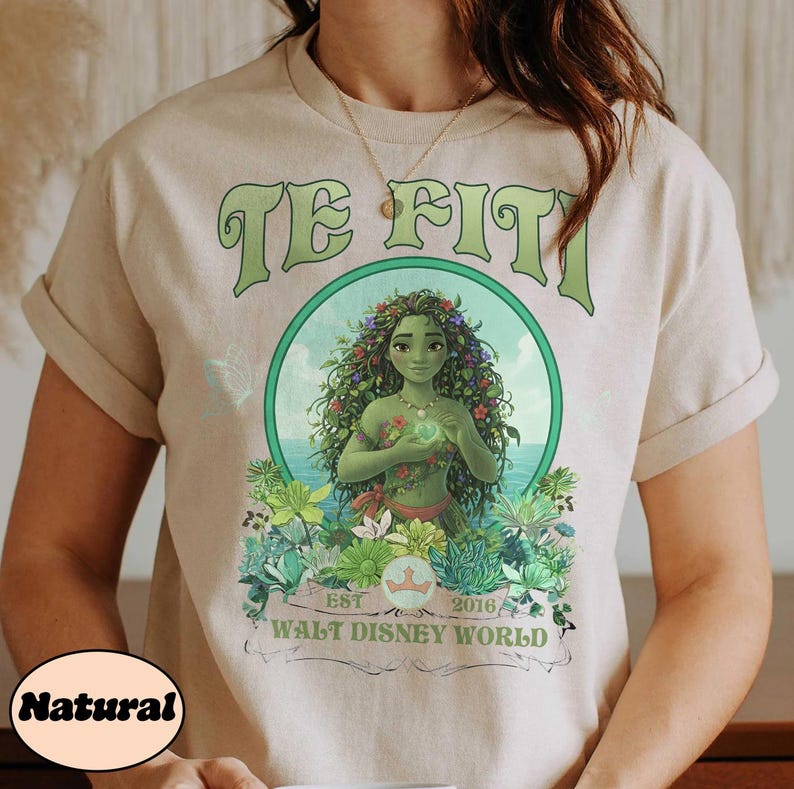 May include: Beige t-shirt featuring a green graphic of Te Fiti from Walt Disney World. The design includes the text "TE FITI" in green, a circular image of Te Fiti, and the text "EST 2016 WALT DISNEY WORLD".