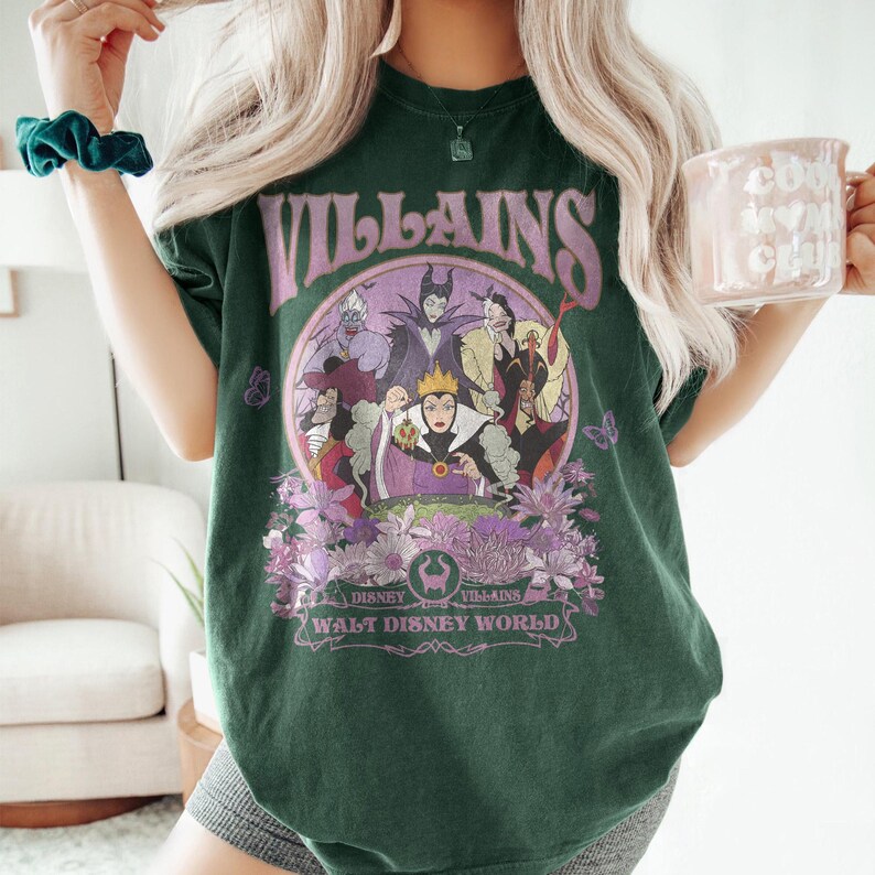 May include: Dark green t-shirt featuring a graphic of Disney villains in a circular design with the word "VILLAINS" above. The design includes the text "Disney Villains Walt Disney World" below the image. The shirt has a relaxed fit.