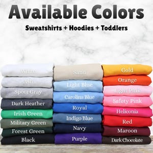 May include: Image showcasing a variety of folded sweatshirts and hoodies in various colors. The text "Available Colors" is at the top, with "Sweatshirts + Hoodies + Toddlers" below. Colors include white, black, red, orange, and more.