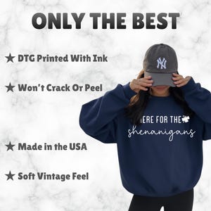 May include: Navy blue sweatshirt with the text "HERE FOR THE shenanigans" in white script. The image also includes the text "ONLY THE BEST", "DTG Printed With Ink", "Won't Crack Or Peel", "Made in the USA", and "Soft Vintage Feel". A gray baseball cap is also visible.
