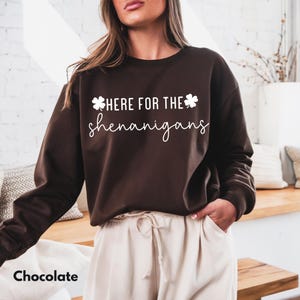 May include: Chocolate brown sweatshirt with the text "HERE FOR THE shenanigans" in white script. The sweatshirt has a crew neck and long sleeves. The word "Chocolate" is at the bottom left of the image.