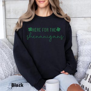 May include: Black sweatshirt with the text "HERE FOR THE shenanigans" in green script and a green shamrock. The word "Black" is printed at the bottom left of the sweatshirt. The sweatshirt is a crew neck style.