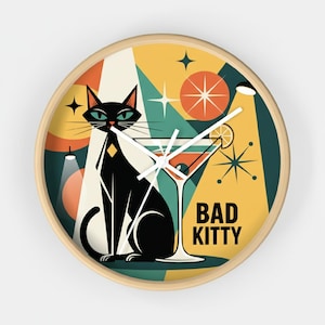 Op de afbeelding: Een ronde wandklok met een retro-ontwerp. Het toont een zwarte kat met groene ogen, een martini glas en de tekst "BAD KITTY". De achtergrond heeft gele, oranje en teal geometrische vormen, met een licht houten frame.