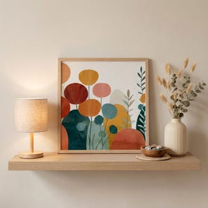 May include: A framed art print with a colorful floral design in shades of red, orange, pink, and blue. The artwork is displayed on a wooden shelf, alongside a small lamp and a vase with dried flowers. The overall aesthetic is modern and minimalist.