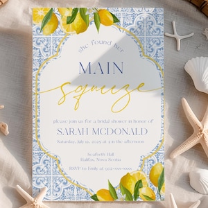 Könnte beinhalten: Eine Einladung zur Brautparty mit einem Zitronen- und blau gefliesten Design, mit dem Text "she found her MAIN squeeze" in goldener Schrift. Die Einladung ist von Muscheln und Seesternen umgeben, die auf einem gewebten Bambustablett angeordnet sind.