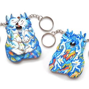 May include: Two keychains featuring colorful wolf designs. One keychain depicts two wolves embracing, while the other showcases a geometric pattern with wolf-like figures. Both keychains have silver key rings and chains.