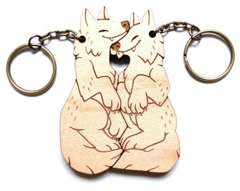 Puede incluir: Llavero de madera con dos lobos abrazándose, con una forma de corazón en el medio. El llavero está hecho de madera marrón claro y tiene una cadena de metal dorado.