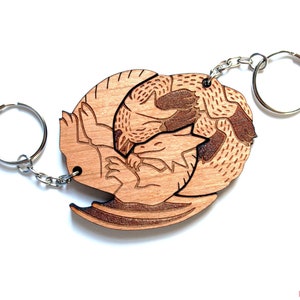 May include: Wooden keychain featuring a laser-engraved design of two dragons intertwined. The keychain is made of light brown wood and has a silver metal ring.