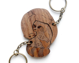 Könnte beinhalten: Ein Holzschlüsselanhänger mit zwei sich umarmenden Faultieren, mit brauner Holzmaserung und einem Schlüsselring aus Messing.